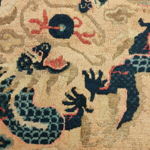 Closeup of a textured tan rug with dark blue, aqua, and coral stylized dragon motifs.
