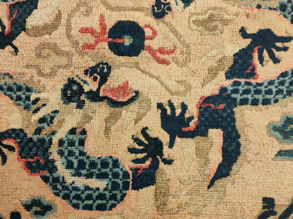 Closeup of a textured tan rug with dark blue, aqua, and coral stylized dragon motifs.