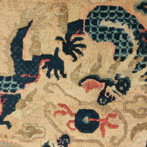 Close-up of a textured rug showing stylized navy, teal, and coral abstract patterns on a tan background.
