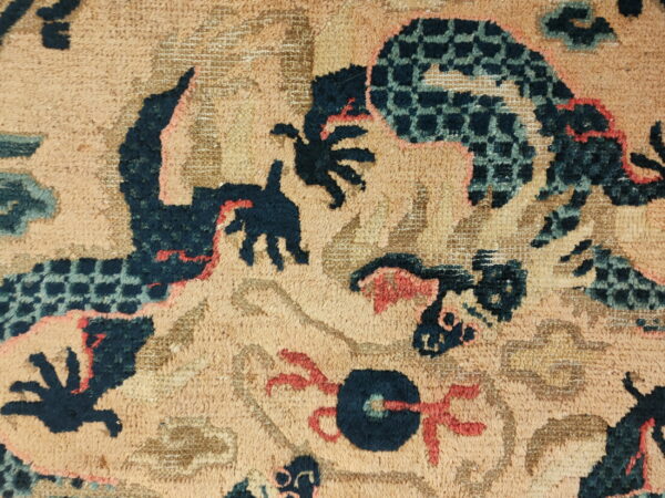 Close-up of a textured rug showing stylized navy, teal, and coral abstract patterns on a tan background.