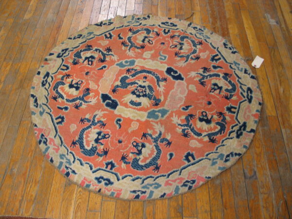 Round orange and blue dragon-patterned rug rests on distressed wood flooring.