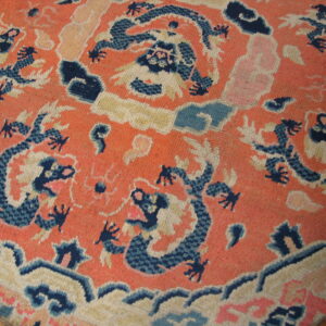 Round orange rug with elaborate dark blue and beige dragon pattern resting on wood floor.