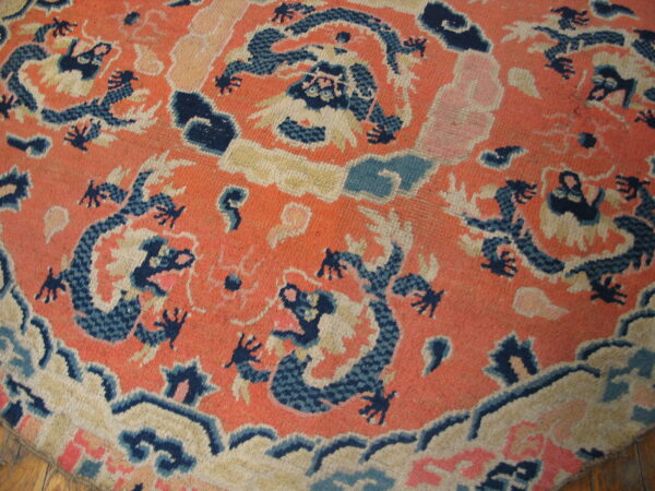 Round orange rug with elaborate dark blue and beige dragon pattern resting on wood floor.