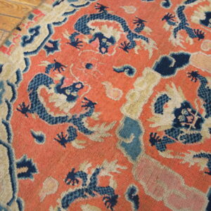Rounded low-pile rug in coral and navy blue with a dragon pattern on wooden plank flooring.