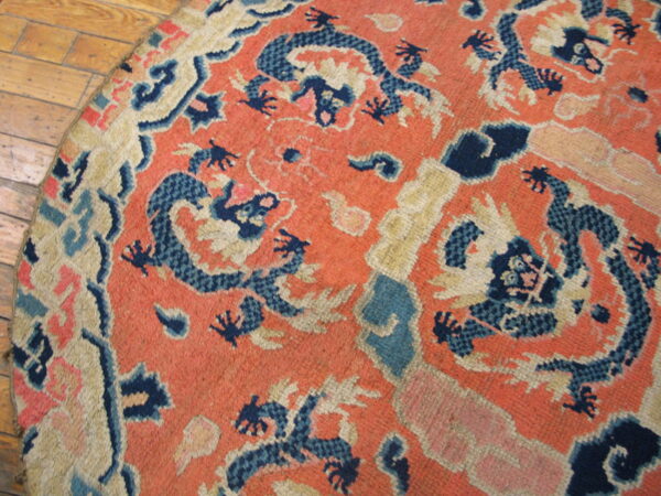 Rounded low-pile rug in coral and navy blue with a dragon pattern on wooden plank flooring.