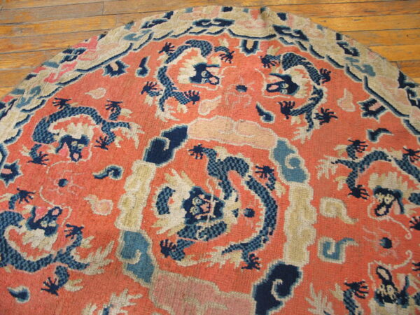 Semicircular coral rug with dark blue and cream stylized patterns sits on wood plank flooring.