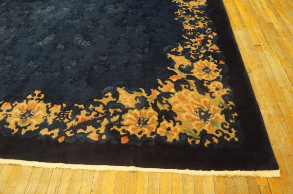High-pile navy rug with carved gold and rust floral border resting on yellow wood planks.
