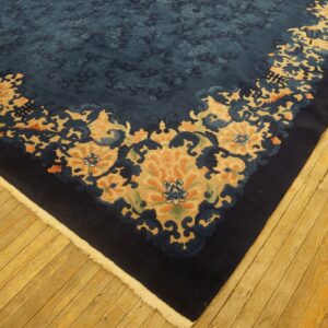 A dark blue floral rug with tan and orange accents lies on rustic, golden-toned wood flooring.