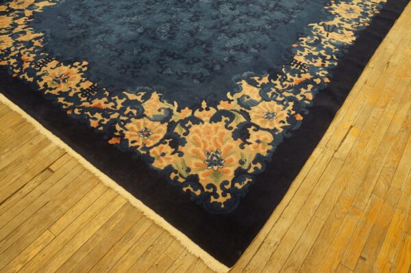 A dark blue floral rug with tan and orange accents lies on rustic, golden-toned wood flooring.