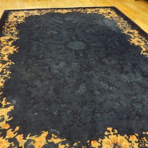 A dark blue rug features a subtle tone-on-tone field and a thick scrolling gold and orange floral border.