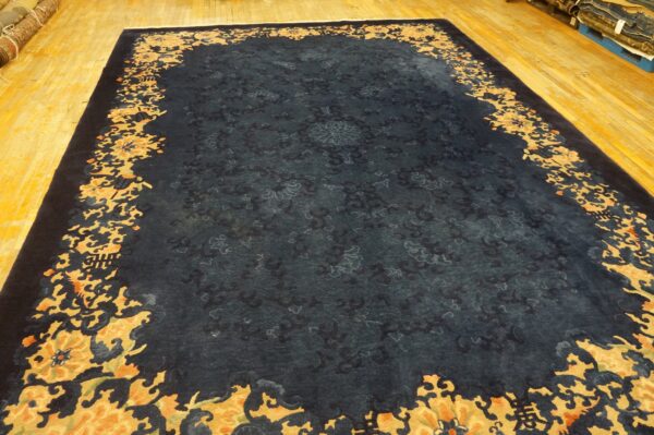A dark blue rug features a subtle tone-on-tone field and a thick scrolling gold and orange floral border.