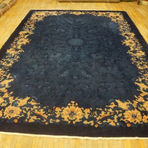 Dark blue rug with a wide gold and peach floral border rests on honey-colored wood flooring.