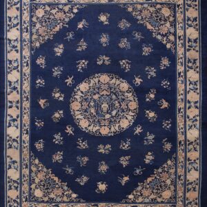 Rectangular dark blue rug with intricate pale pink and blue floral patterns and wide decorative borders.