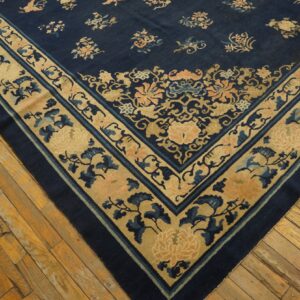 Navy blue rug featuring beige and peach floral borders and motifs rests on worn hardwood flooring.