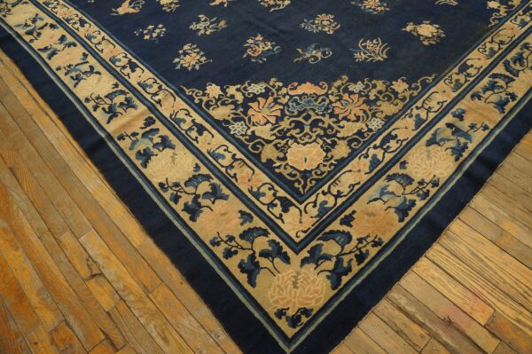 Wool hand knotted pile blue antique rectangle 1890s rug 3 Navy blue rug featuring beige and peach floral borders and motifs rests on worn hardwood flooring.