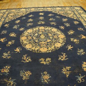 Large low-pile dark blue rug with intricate pale yellow and blue patterns displayed on wooden flooring.