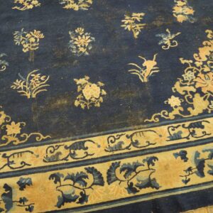 Low-pile rug in navy blue and gold with traditional floral patterns resting on a light wood floor.