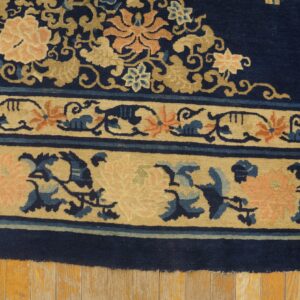 Close-up of a dark blue rug with beige floral borders and pink accents on distressed wood planks.