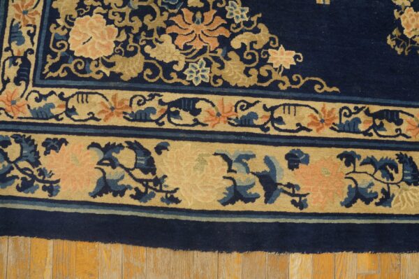 Wool hand knotted pile blue antique rectangle 1890s rug 7 Close-up of a dark blue rug with beige floral borders and pink accents on distressed wood planks.