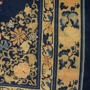 Navy blue rug features peach and tan floral scrollwork and detailed borders on light-toned hardwood floors.