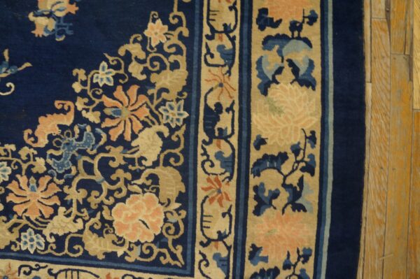 Wool hand knotted pile blue antique rectangle 1890s rug 8 Navy blue rug features peach and tan floral scrollwork and detailed borders on light-toned hardwood floors.