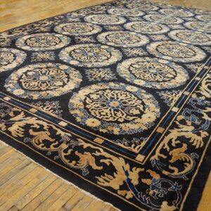 Navy blue rug with repeating tan and blue medallion patterns covers wide plank wood flooring.