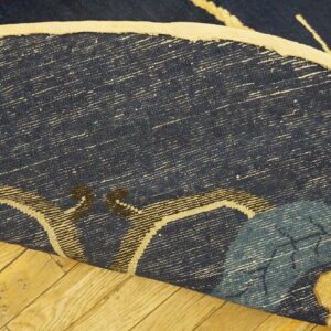 Navy blue rug backing with white weft threads and light binding curls over yellow wood planks.