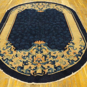 Oval navy blue rug featuring a detailed tan and coral floral border rests on bright yellow hardwood flooring.