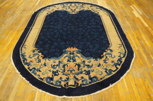 Oval navy blue rug featuring a detailed tan and coral floral border rests on bright yellow hardwood flooring.