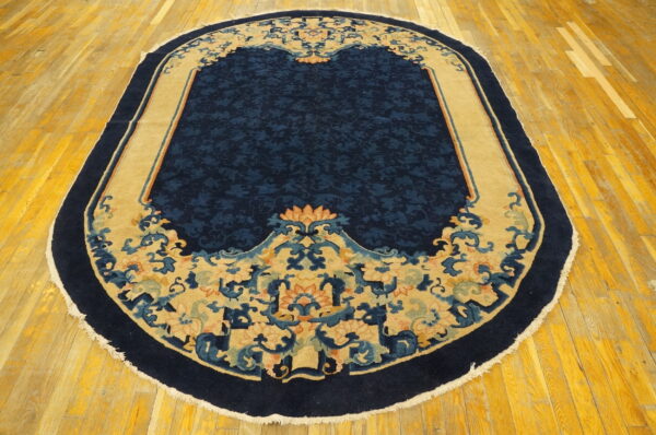 Navy blue oval rug with a stylized tan and multicolor floral border on golden hardwood.