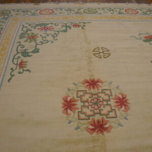 Cream rug with a colorful floral and vine border and scattered red and green motifs on wood flooring.