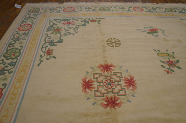 Cream rug with a colorful floral and vine border and scattered red and green motifs on wood flooring.