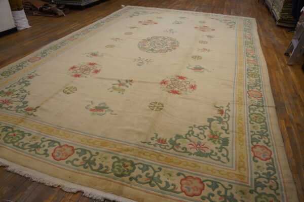 Pale cream rug with scattered pastel floral motifs and geometric medallions, resting on wide wooden planks.