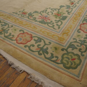 The carved border of a cream and multicolored floral rug rests on rustic wood flooring.