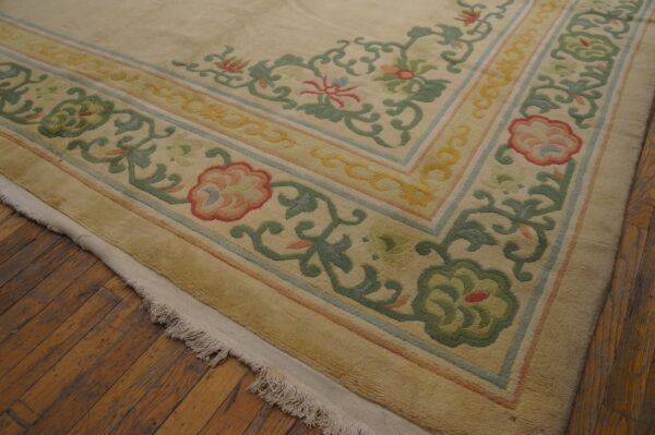 The carved border of a cream and multicolored floral rug rests on rustic wood flooring.