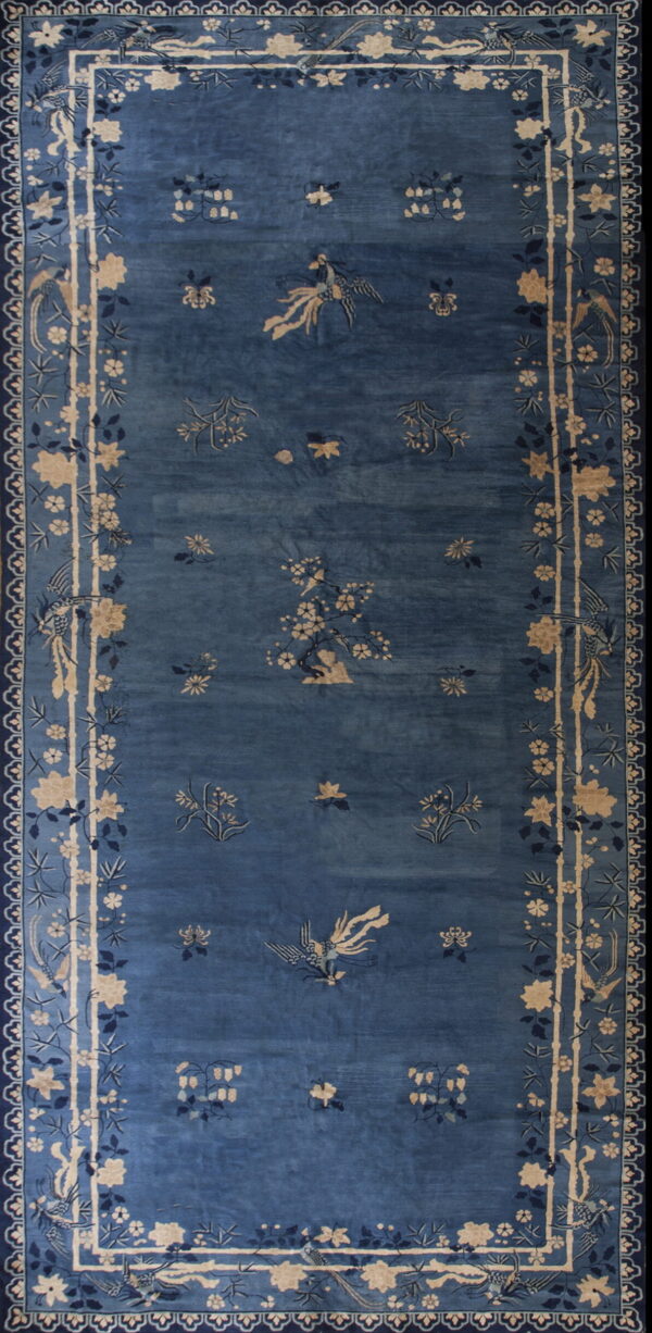 Long blue rug with visible sheen, patterned with tan florals and exotic birds in the field and border.