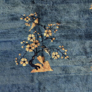 Textured deep blue rug featuring a golden-tan motif of a blossoming tree and birds.
