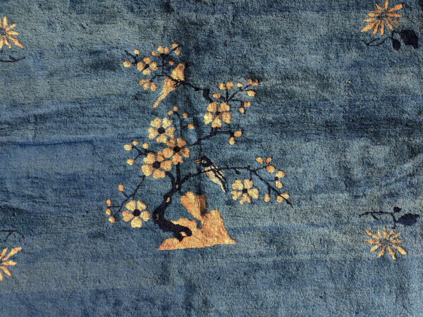 Textured deep blue rug featuring a golden-tan motif of a blossoming tree and birds.