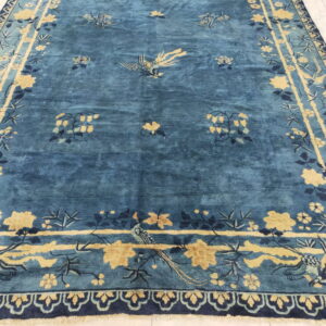 Deep blue rug with gold and navy botanical and bird patterns rests on a white tiled floor.