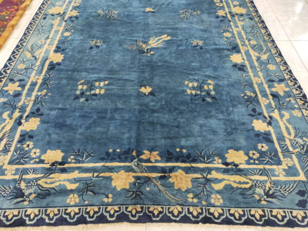 Deep blue rug with gold and navy botanical and bird patterns rests on a white tiled floor.