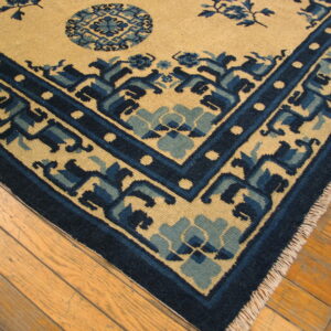 Tan and blue rug corner showing geometric borders and fringe on light hardwood flooring.