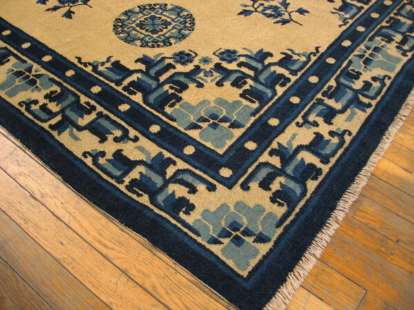 Tan and blue rug corner showing geometric borders and fringe on light hardwood flooring.