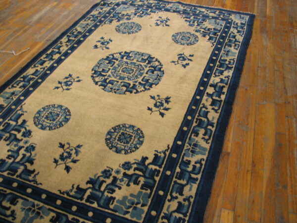 Beige and blue traditional rug with medallions and intricate borders lying on worn wood planks.