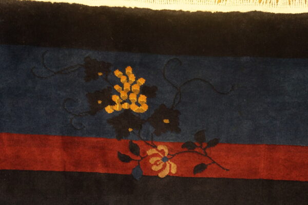 Dark blue, red, and black striped rug detail with orange and tan floral motifs and white fringe.