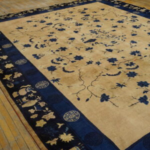 Oversize tan rug featuring scattered blue floral motifs and a complex navy pictorial border on wood flooring.