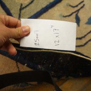 Hand holding paper over a beige and dark blue floral rug resting on wood floor.