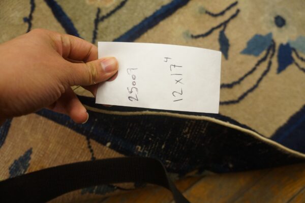 Hand holding paper over a beige and dark blue floral rug resting on wood floor.