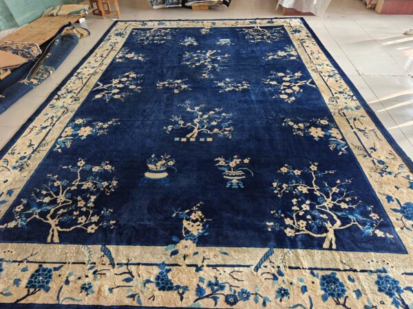 Large blue rug with a beige border and flowering tree patterns, displayed on white tile floor.
