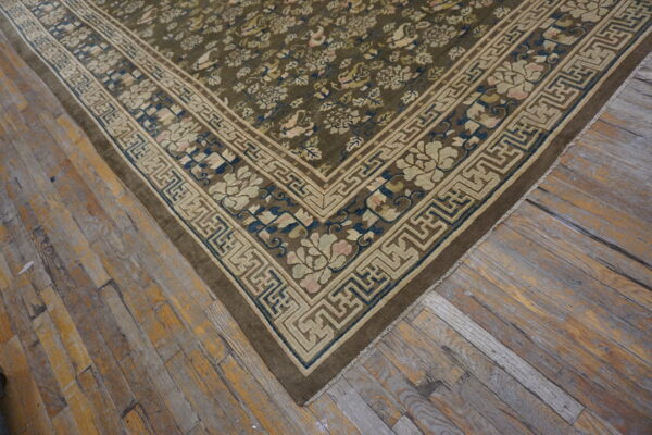 Olive green rug with ornate floral and geometric borders placed on distressed wooden floorboards.
