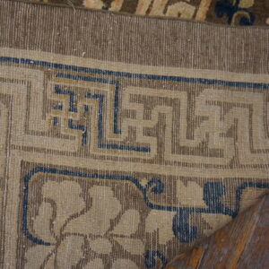 Low-pile rug corner featuring tan, brown, and blue geometric and floral patterns on wood floors.